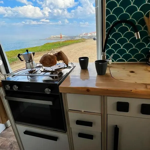 Cocina de camper con horno y fogón junto a la puerta abierta al mar
