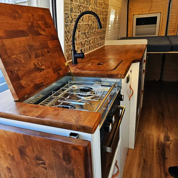 Cocina de camper con tapa de madera abierta, fogón y fregadero