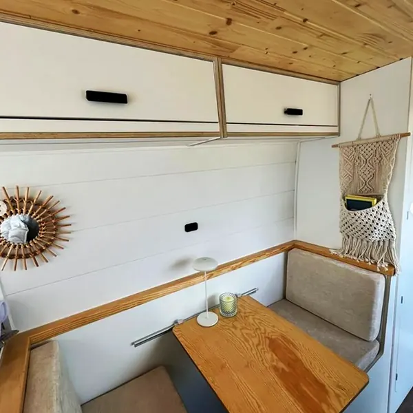 Dinette de camper con mesa de madera, armarios blancos y detalles de macramé