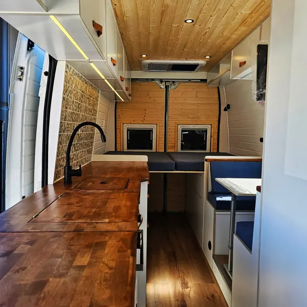 Interior de camper con cocina de madera, dinette y cama al fondo