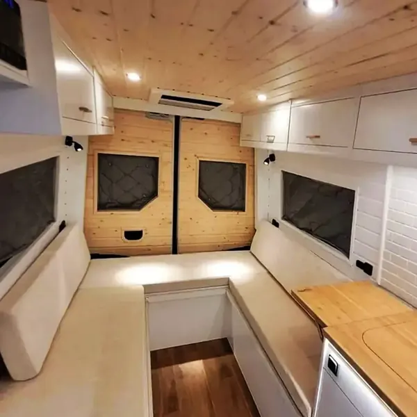 Interior de camper en madera clara con armarios altos y ventanas